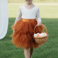 Flower girl dress in burnt orange tiered tutu style tulle with long white lace sleeves. 