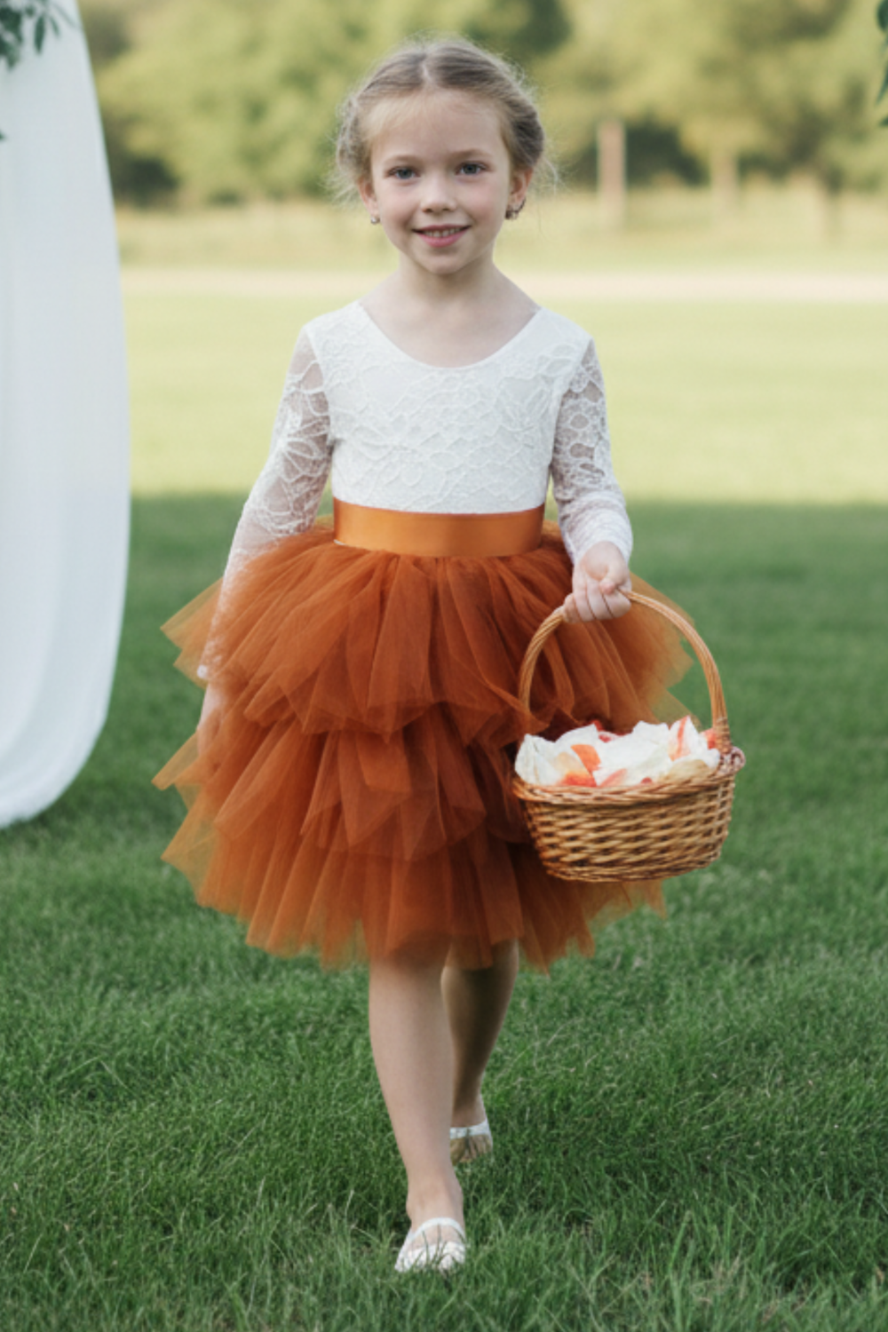 Flower girl dress in burnt orange tiered tutu style tulle with long white lace sleeves. 