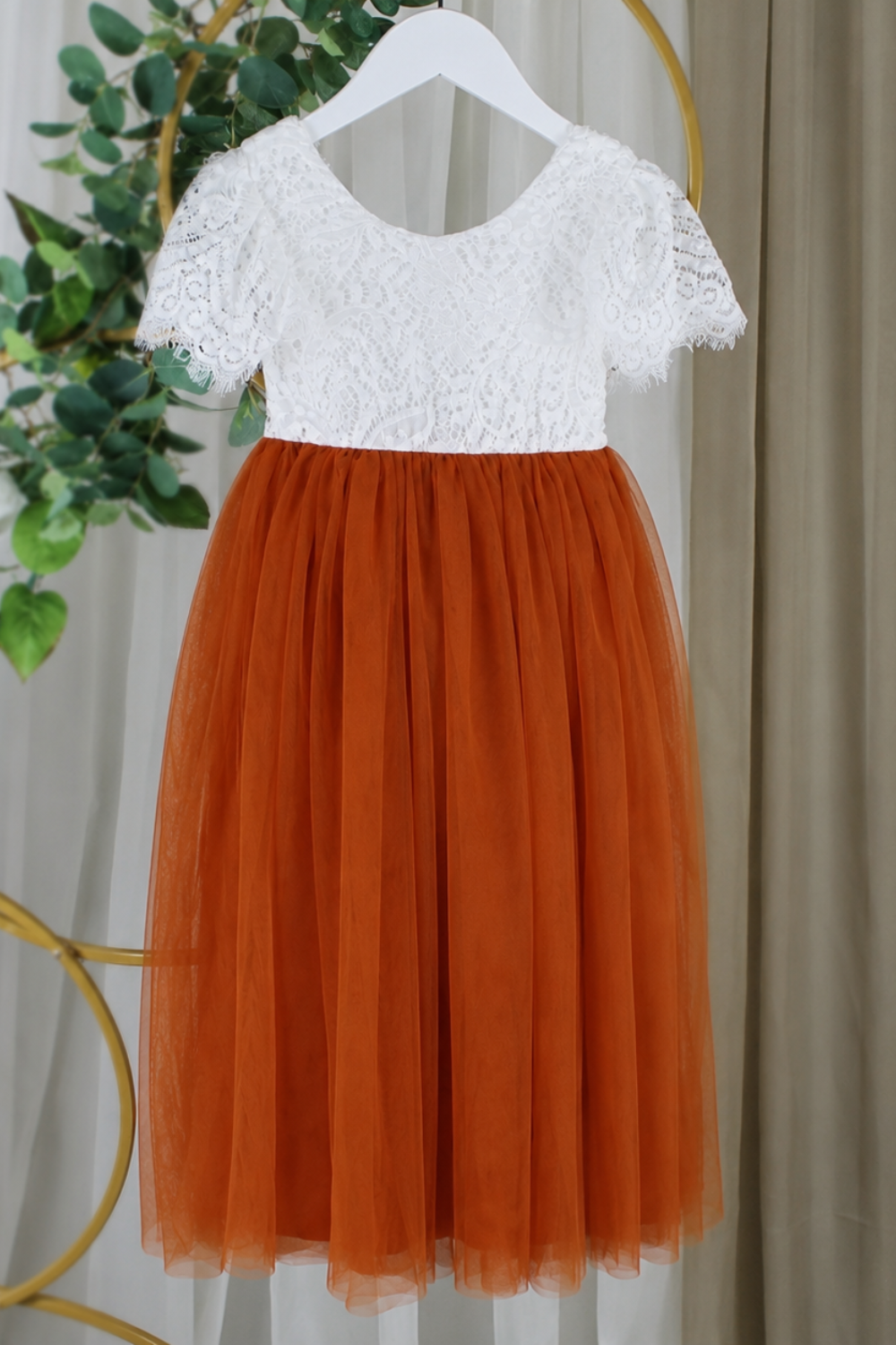 Orange flower girl dress shown from the back with white lace and satin sash