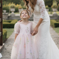 flower girl dress in light pink floral embroidery with big puffy sleeves and big tie bow in back. 